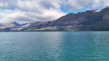 Parçalı bulutlu bir gökyüzünün altında görkemli dağları olan sakin bir göl. Sakin sular Yeni Zelanda, Glenorchy 'nin doğal güzelliğini yansıtır.