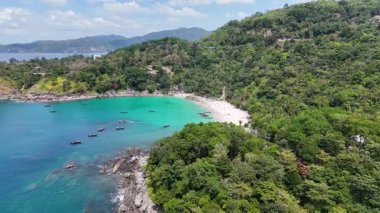 Hava görüntüleri Phuket, Tayland 'da sakin bir sahil koyunu görüntüler, turkuaz sular, yemyeşil alanlar ve açık gökyüzü altında dağınık tekneler sergilenir.