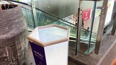 Modern bir alışveriş merkezindeki çöp kutusuna çöp atan biri. Parlak aydınlatma ve temiz ortam sorumlu atık imhasını vurguluyor