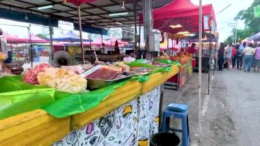 Kanchanaburi, Tayland 'da canlı kırmızı gölgeler altında renkli tezgahlar ve taze ürünlerle hareketli pazar sahneleri