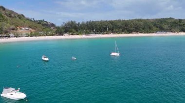 İnsansız hava aracı görüntüleri, sakin Phuket kıyılarını kayıklar ve yemyeşil alanlarla, sakin turkuaz suları ve kumlu plajları görüntülüyor.