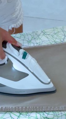 Parlak, doğal ışıklandırmada buhar ütüsü kullanan bir insan desenli bir tahtada pantolonunu ütüler.