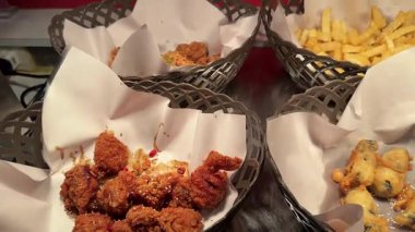 Market tezgahındaki sepetlerde çeşit çeşit kızarmış atıştırmalıklar. Ilık ışıklandırma çıtır çıtır dokuları ve canlı renkleri vurgular