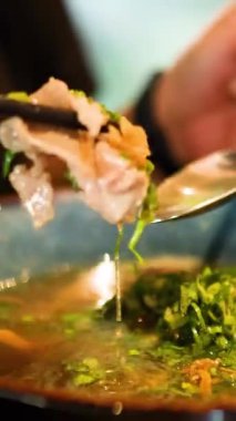 Yakın plan yemek çubukları ve kaşık, canlı ve sıcak bir restoran ortamında erişte ve et tutuyor.