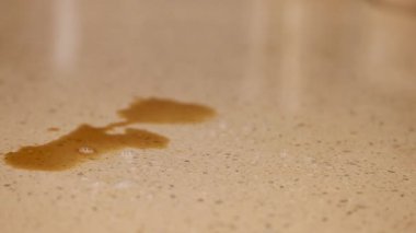 Bir el, sıcak aydınlatma altında, bir bez kullanarak, bir tezgahın üzerine dökülen kahveyi siler.