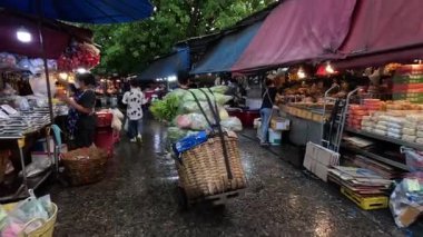 Yağmurlu bir açık hava pazarında müşteriler ve satıcılar meşgul.