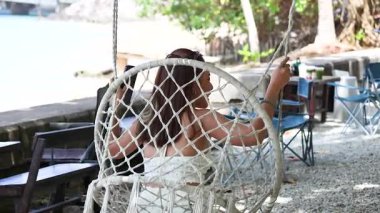 Bir kadın Sarasin Köprüsü yakınlarındaki bir salıncakta huzurlu bir anın tadını çıkarır, Phuket. Doğal ışıklandırma ve dingin çevre sakinliği arttırır.