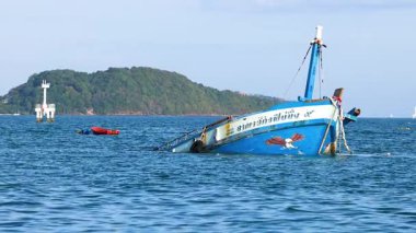 Tayland, Phuket yakınlarındaki okyanusta bir balıkçı teknesi yavaş yavaş batıyor, açık gökyüzünün altında, çevresindeki adalar görülebiliyor.
