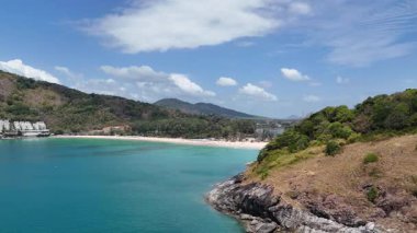 Drone görüntüleri, Phuket 'in kıyı şeridinin sakin bir üstgeçidini, turkuaz sularını, yemyeşil sularını ve berrak gökyüzünün altında demirlemiş yatları yakalıyor.