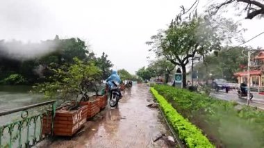 Motosikletli yağmurlu Hanoi caddesinde gidiyor.