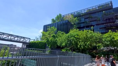 İnsanlar Bangkok, Tayland 'da aydınlık gün ışığında yemyeşil verimli bir mimariyle modern mimarinin yanından geçiyor.