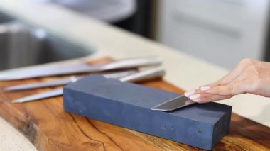 Bir insan, iyi aydınlatılmış bir mutfakta bıçağını bileyerek teknik ve hassasiyete odaklanır.