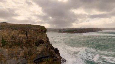 Drone görüntüleri Avustralya 'nın Port Campbell kentindeki bulutlu gökyüzünün altında dramatik kayalıkları ve çalkantılı okyanus dalgalarını yakalıyor.