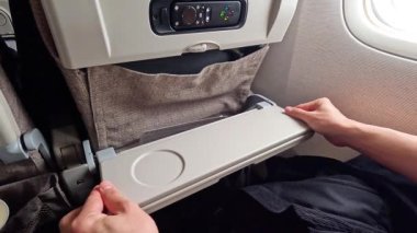 Koltuktaki uçak tepsisini katlayan kişi