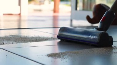 Elektrikli süpürge, güneşli fayans zeminindeki döküntüleri etkili bir şekilde temizler ve modern ev bakımını ön plana çıkarır.