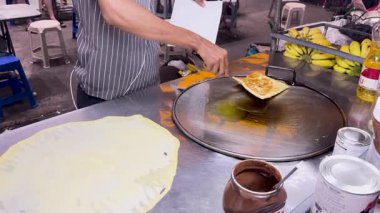 Phuket 'teki bir sokak satıcısı Tayland roti' sini sıcak bir ızgaraya hazırlıyor, geleneksel sokak yemekleri tekniklerini canlı ışıklandırmada sergiliyor.