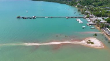 Hava görüntüleri Phuket 'in canlı sahil şeridini, turkuaz suları, kumlu plajları ve tekneli hareketli bir iskeleyi görüntüler.