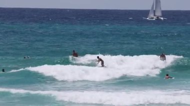 Açık bir günde dalgaları yakalayan birden fazla sörfçü
