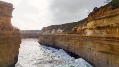 Avustralya 'daki Port Campbell, Loch Ard Gorge' daki engebeli uçurumların ve okyanus dalgalarının hava görüntüleri. Bulutlu aydınlatma dramatik manzarayı güçlendirir