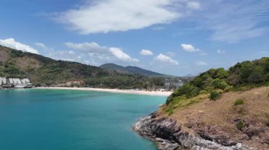 Drone görüntüleri, Phuket 'in kıyı şeridinin sakin bir üstgeçidini, turkuaz sularını, yemyeşil sularını ve berrak gökyüzünün altında demirlemiş yatları yakalıyor.