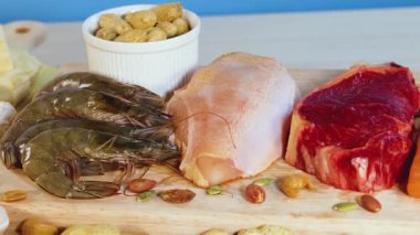 Parlak ışıklandırmalı ahşap bir yüzeye yerleştirilmiş et, fındık, süt ürünleri ve deniz ürünleri de dahil olmak üzere protein zengini gıdaların canlı bir gösterisi