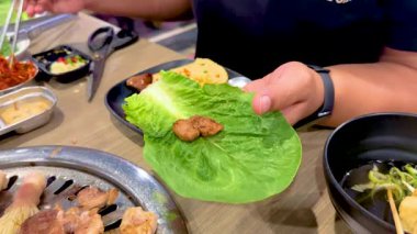 Eller canlı bir Bangkok ortamında ızgara et ve sebzeli Kore mangalı marul sarması hazırlasın.