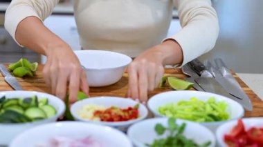 Eller, iyi aydınlatılmış mutfak ortamında ahşap bir tahtaya taze sebze ve malzeme diziyor.