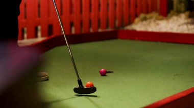 Bir golf sopası mini golf sahasında sıcak ışık altında renkli bariyerler olan bir golf topuna vurur.