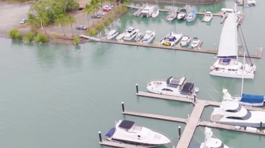 Queensland, Port Douglas 'taki bir marinaya yanaşmış yatların hava görüntüleri. Parlak gün ışığı dingin suyu ve çevreleyen yeşilliği vurgular