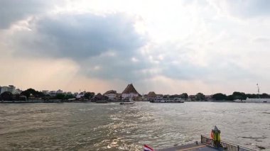 Tayland, Bangkok 'taki Chao Phraya Nehri' nin sakin bir sahnesinde, yumuşak ve dağınık güneş ışığı altında tekneler ve geleneksel mimari...
