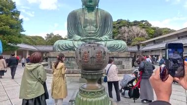 Ziyaretçiler Kotokuin Tapınağı, Kamakura 'daki ikonik Büyük Buda heykelinin canlı yeşil gökyüzünün altında fotoğraflarını çekiyorlar.