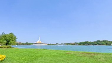 Rama IX Park, Bangkok 'ta sakin bir manzara, yemyeşil, göl ve açık mavi gökyüzünün altında uzak bir pavyon.