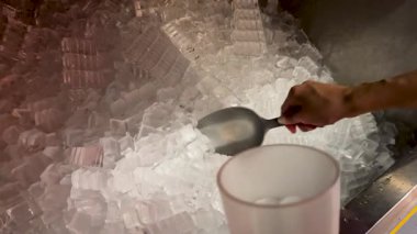 Bir insan loş bir ortamda büyük bir buz kutusundan buz topluyor.