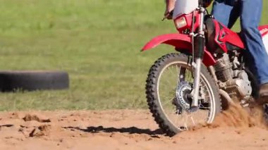 Motosikletçi toprak yolda gösteri yapıyor.