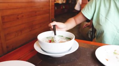 Ahşap bir masada erişte çorbası içen biri.