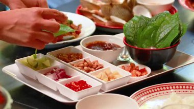 Miang Kham 'ı Phuket' teki bir masada taze malzemelerle birleştiren eller. Parlak ışıklandırma yemeğin canlı renklerini güçlendirir