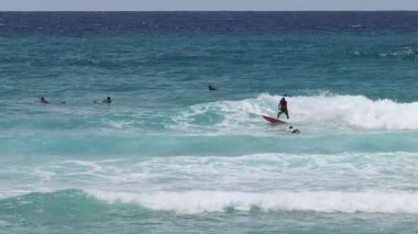 Bir sörfçü diğerleriyle birlikte bir dalgaya biner..