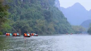 Tekneler, yemyeşil dağlarla çevrili manzaralı nehirde yol alırlar.