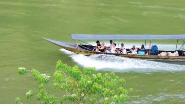 Uzun kuyruklu bir tekne, Kanchanaburi, Tayland 'daki Kwai nehri boyunca hızla ilerler ve canlı atmosferi ve manzarayı yakalar.