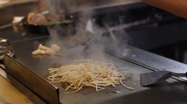 Şef sıcak ızgarada erişte ve et pişiriyor.