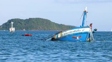 Tayland, Phuket yakınlarındaki okyanusta bir balıkçı teknesi yavaş yavaş batıyor, açık gökyüzünün altında, çevresindeki adalar görülebiliyor.