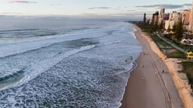 İnsansız hava aracı gündoğumunda sakin Altın Sahil plajını yakalar. Hafif dalgaları ve sabahın erken saatlerini vurgular.