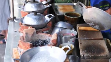 Eller kalabalık bir Phuket pazarında kil sobada hindistan cevizi atıştırmalıkları hazırlar. Parlak ışıklandırma geleneksel yemek pişirme tekniklerini vurguluyor