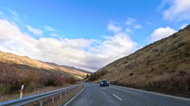 Wanaka, Yeni Zelanda 'da dolambaçlı bir yol boyunca sakin bir yolculuk, canlı bir sonbahar yeşilliği ve açık mavi gökyüzü.
