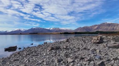 İnsansız hava aracı görüntüleri Tekapo Gölü 'nün sakin sularını ve canlı bir gökyüzü altında kayalık kıyı şeridini yakalar ve Yeni Zelanda' nın doğal güzelliğini gözler önüne serer.