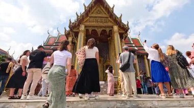 Turistler Bangkok 'ta Wat Phra Kaew' i keşfederek güneşli gökyüzünün altında canlı bir mimari yakaladılar. Sahne canlı ve kültürel olarak zengin.