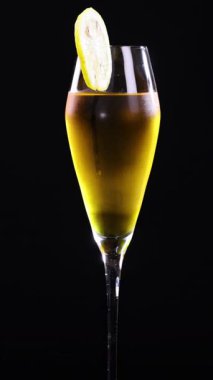 Uzun bardakta limon ekşi kokteyl, limon dilimli garnitür, siyah arka planda.