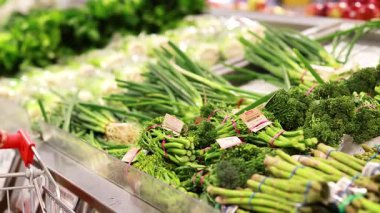 Parlak ışıklı bir süpermarkette taze brokoli ve taze soğan topluyor.