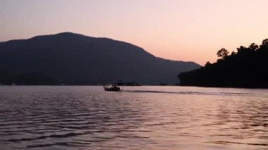 Tekne gün batımında sakin bir gölde ilerliyor.