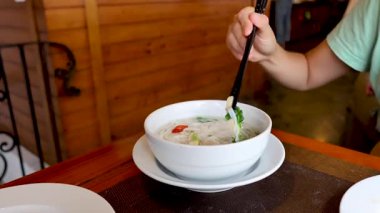 Sofrada çubuklarla erişte çorbası içen biri.